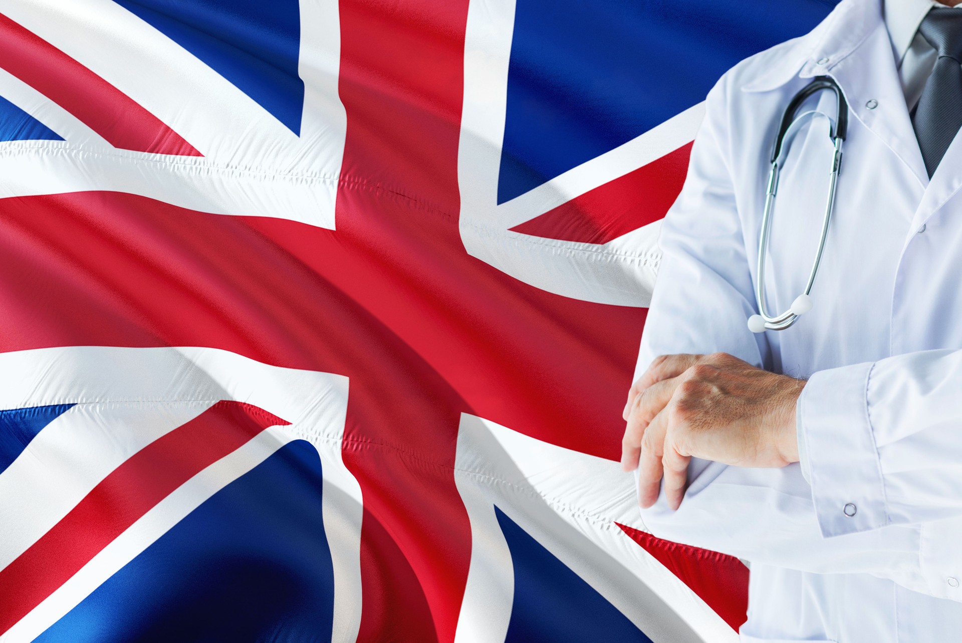 British Doctor standing with stethoscope on United Kingdom flag background. National healthcare system concept, medical theme.British Doctor standing with stethoscope on United Kingdom flag background. National healthcare system concept, medical theme.Bri
