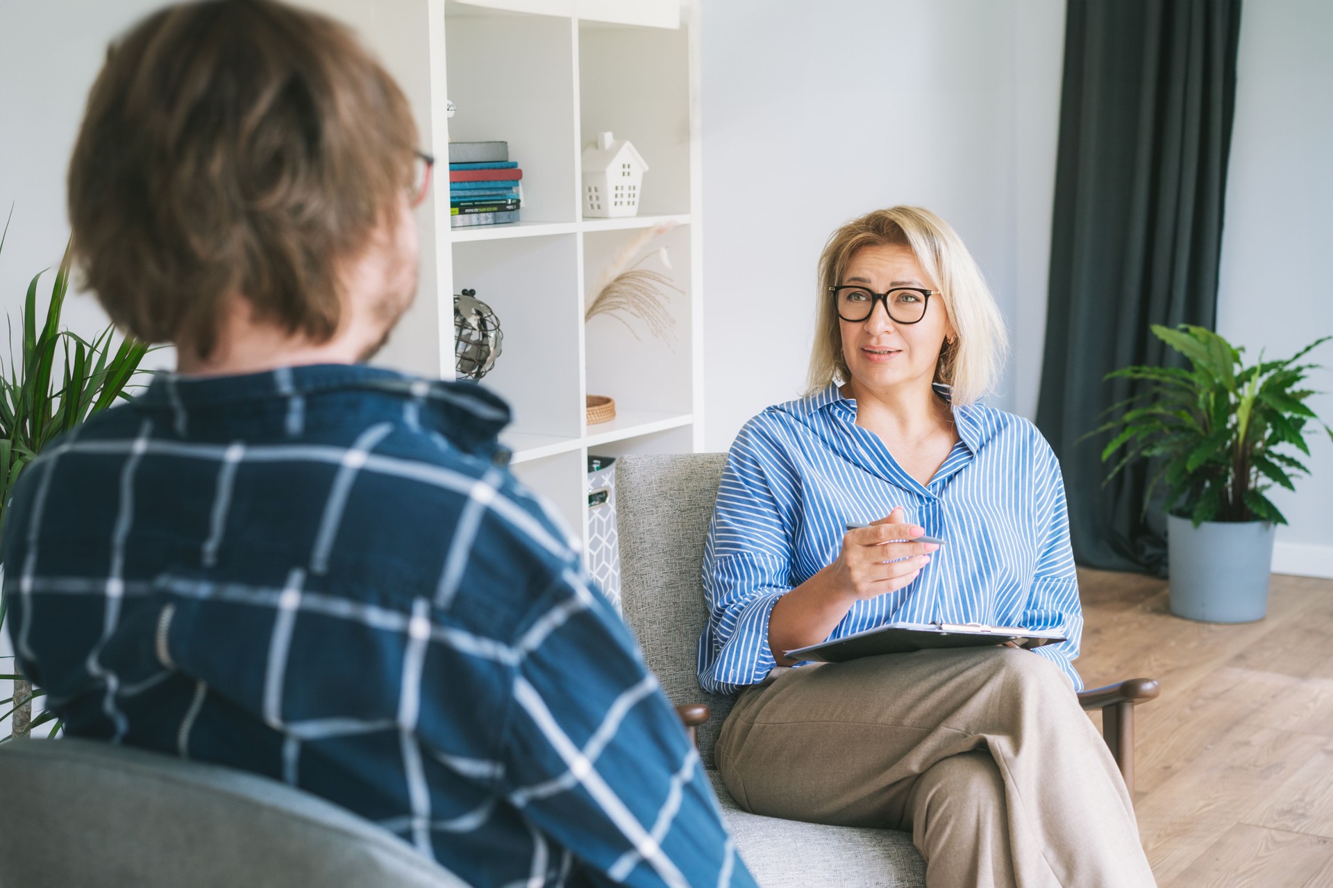 Professional psychotherapy. Female psychologist having session with male patient at mental health clinic, Taking Note During Appointment In Office. Psychological help service. Treatment of depression