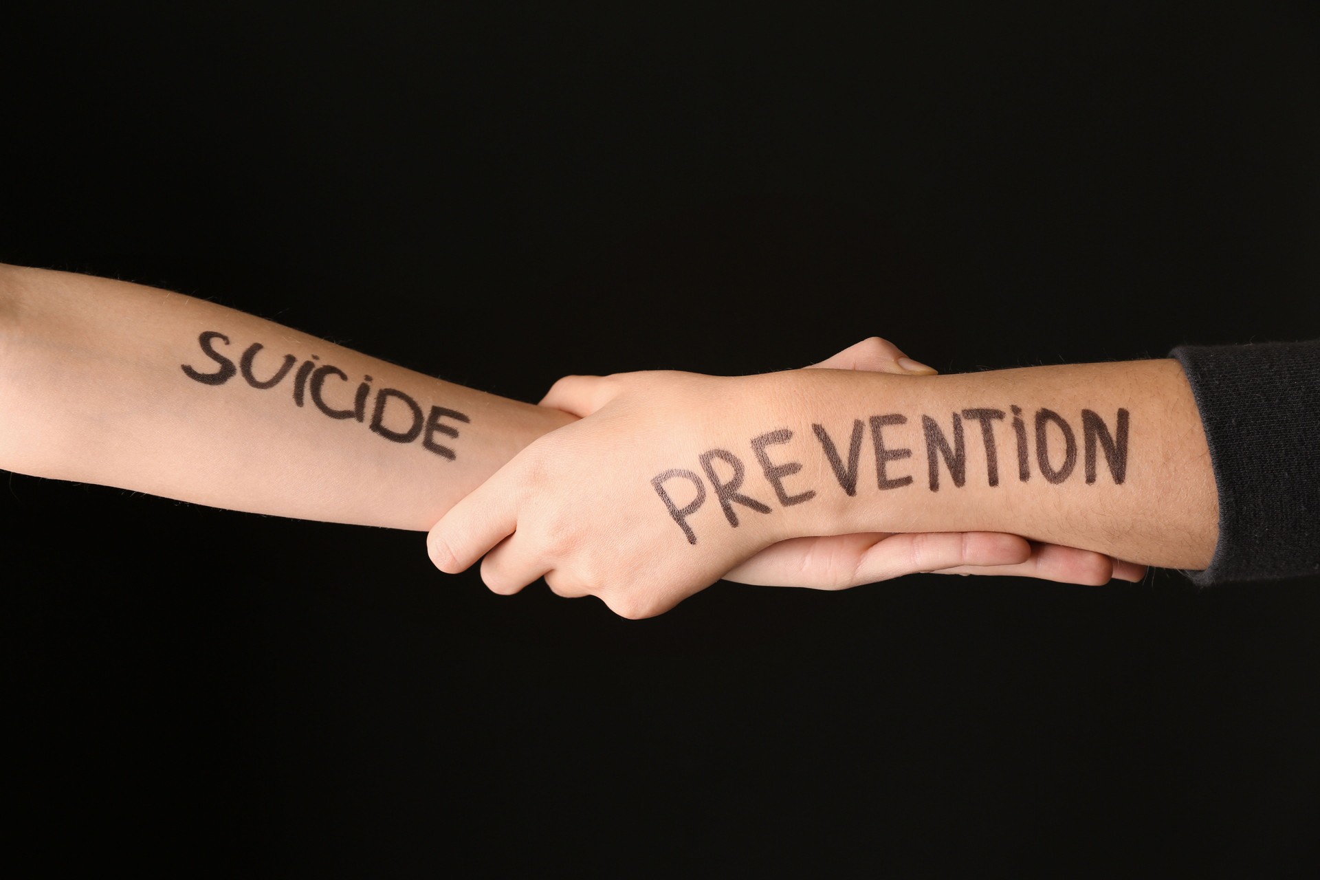 Two hands firmly grasping each other, with SUICIDE and PREVENTION written on their arms